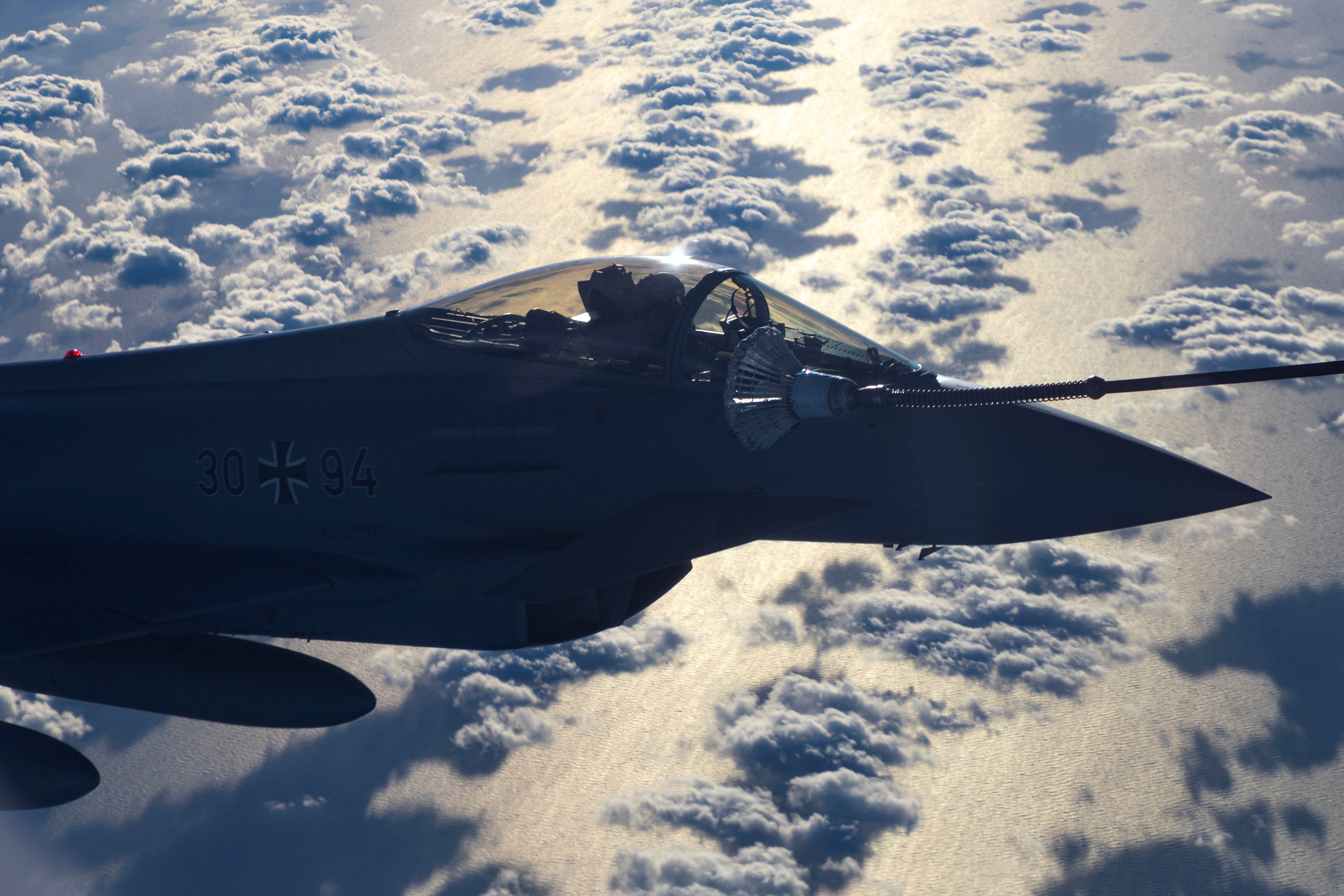 Fighter jet during air-to-air refuelling over the clouds. 